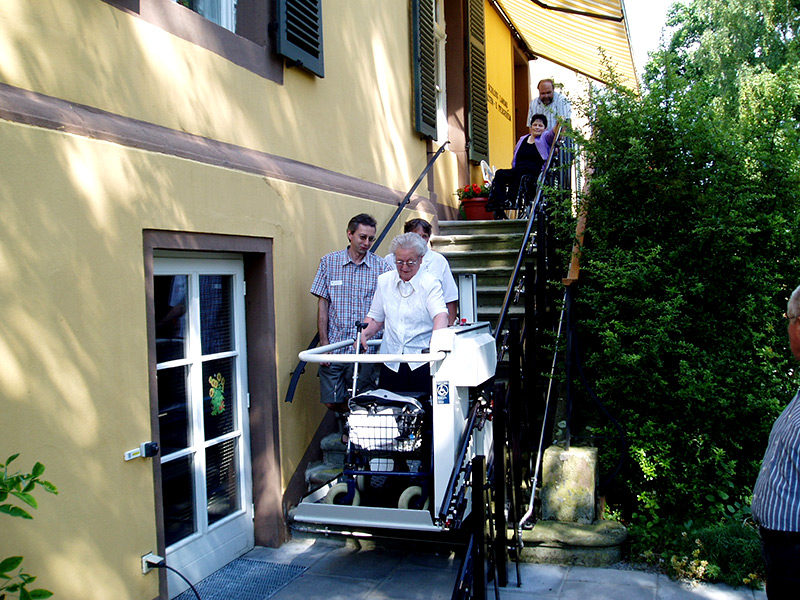 Die AfB Kassel e.V., die AfbM Waldeck - Frankenberg e.V. und die AfbM Hessen e.V. fördern die Mobilität der Bewohner des Alten- und Pflegeheimes Schloss Landau durch die Unterstützung bei der Anschaffung eines Treppenlifters. Die Familie am Treppenlifter